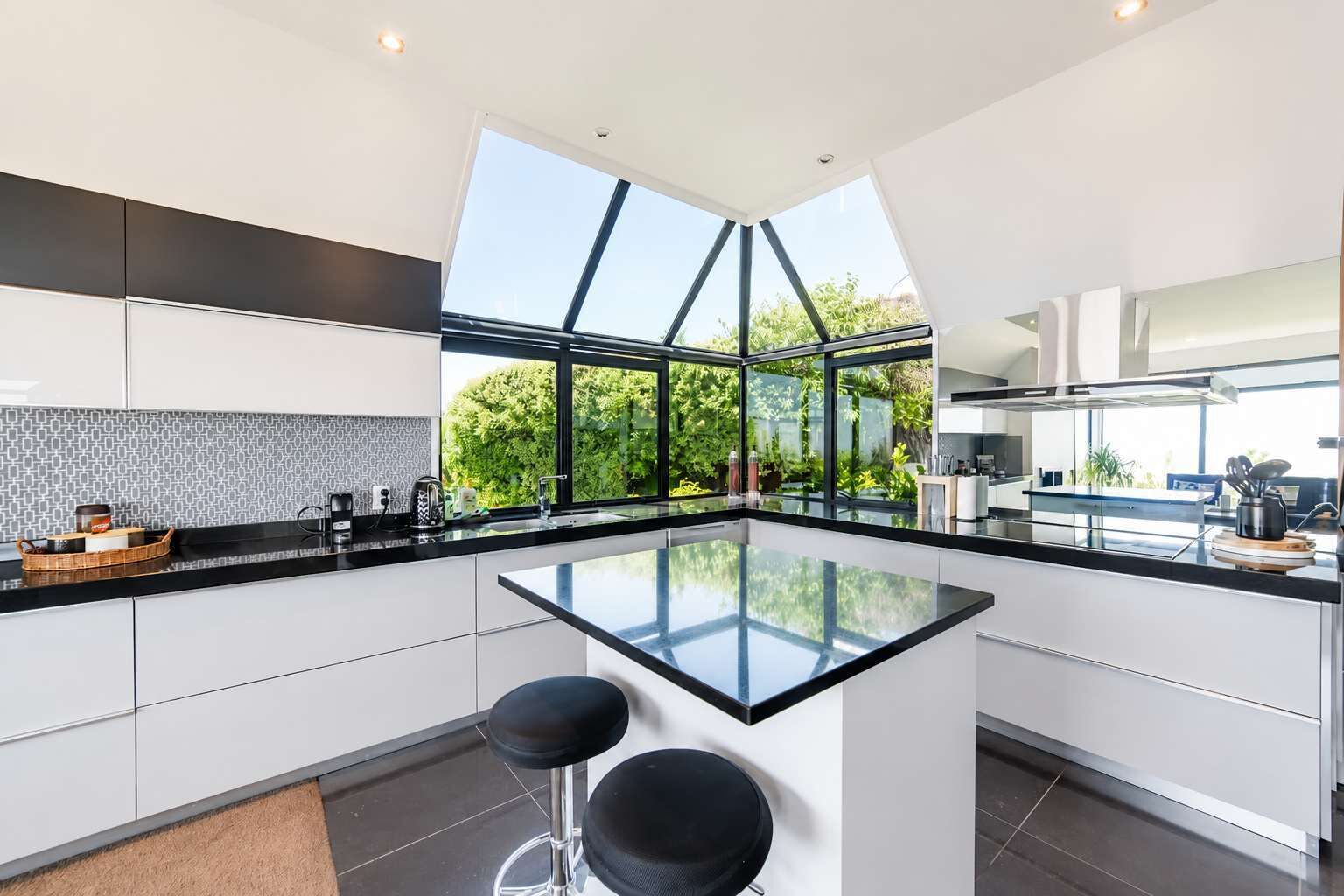 Une cuisine moderne dotée d’un îlot central, de grandes fenêtres et offrant une vue sur la verdure.
