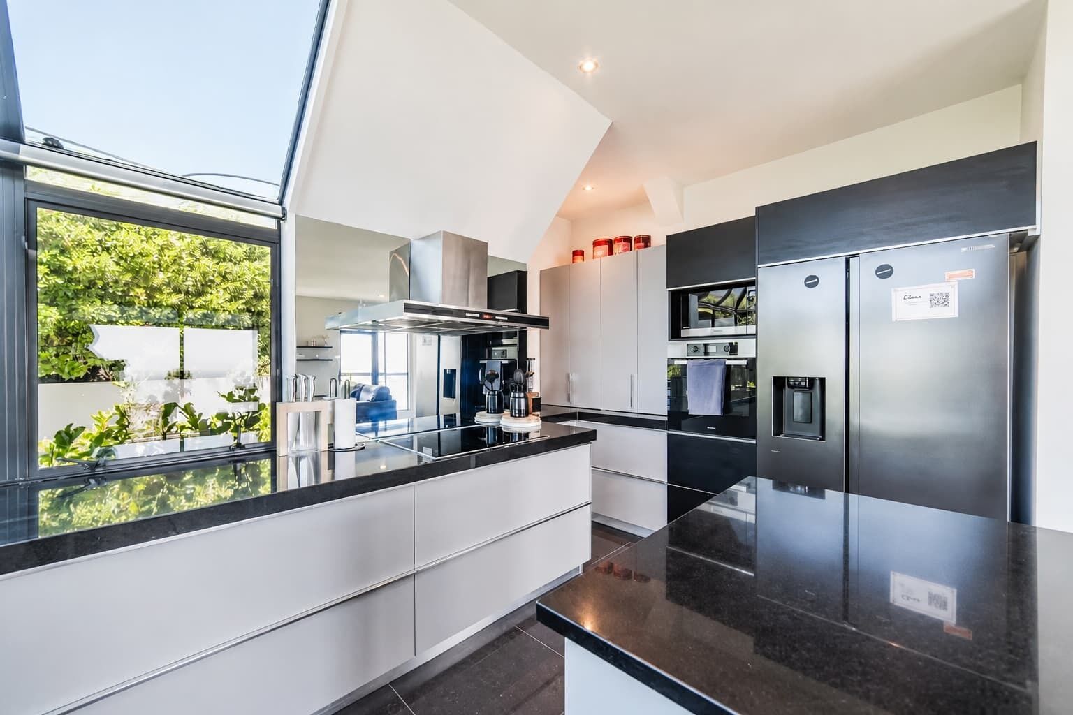 A modern kitchen with a black countertop, stainless steel appliances, and a view of greenery outside.