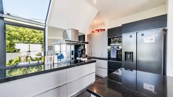A modern kitchen with a black countertop, stainless steel appliances, and a view of greenery outside.