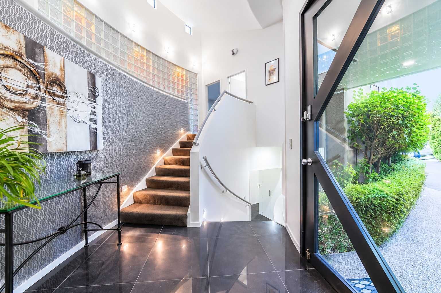 A modern interior with a glass door leading outside, a staircase with a white railing, and a wall with a textured pattern.