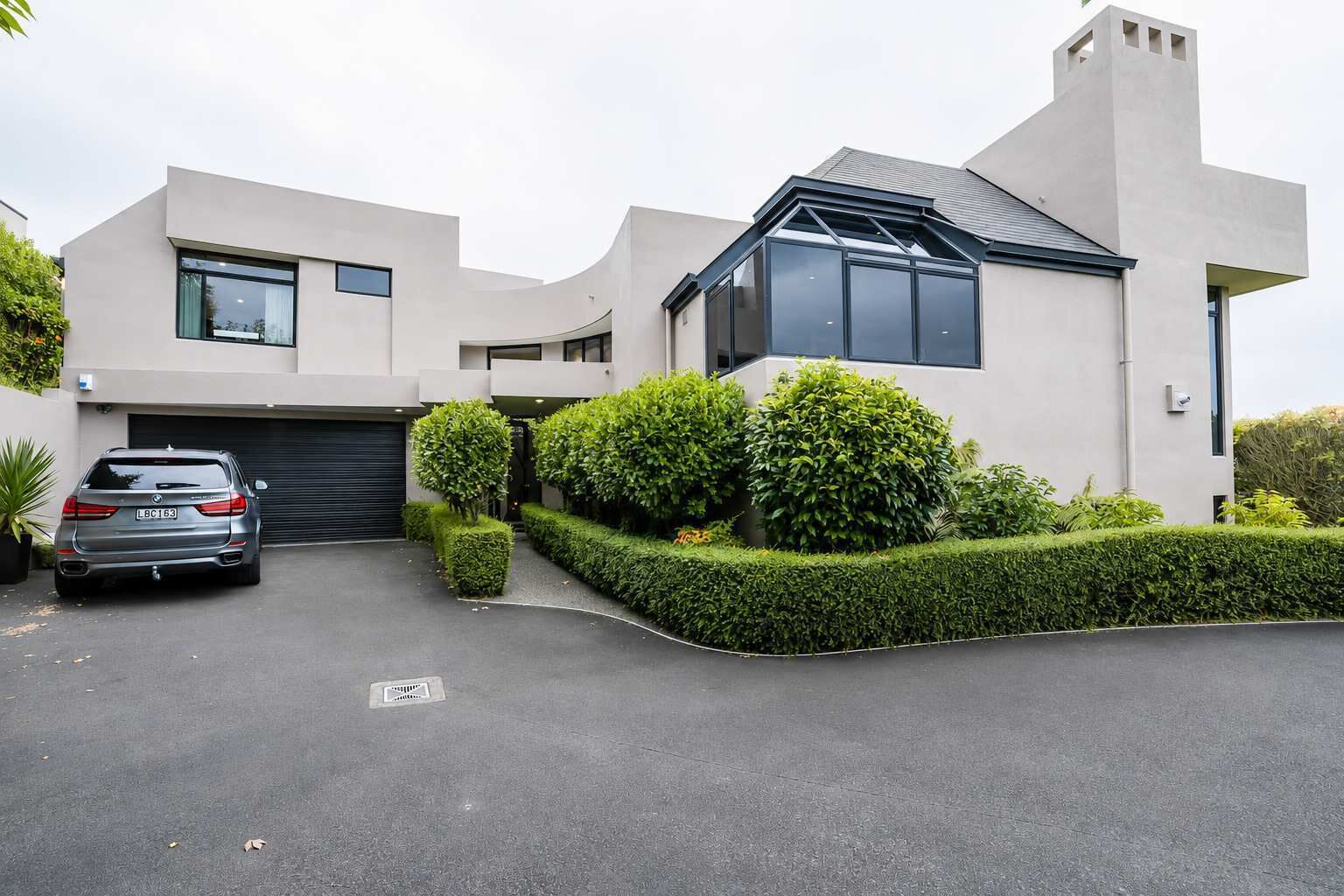 A modern two-story house with a garage, a driveway, and well-maintained hedges.