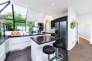 A modern kitchen with a central island, bar stools, and a view of greenery outside.