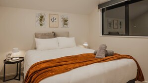 Ein ordentlich eingerichtetes Hotelzimmer mit einem Bett, einem Nachttisch mit Lampe und gerahmten Pflanzenbildern an der Wand.