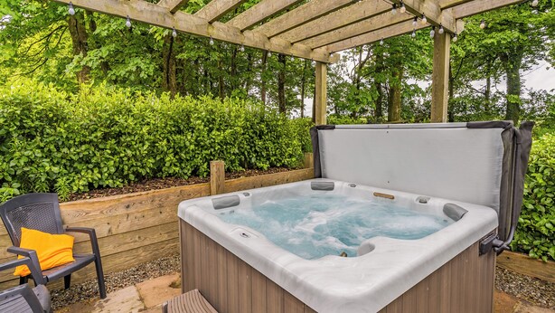 Ett bubbelbad med träpanel på utsidan, en träpergola ovanför och en stol med en gul kudde.