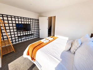 A modern bedroom with a bed, a TV mounted on a black grid wall, and a wooden ladder.