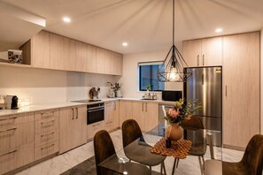 Une cuisine moderne avec des meubles en bois, un réfrigérateur en acier inoxydable et un coin repas comprenant une table et des chaises en verre.