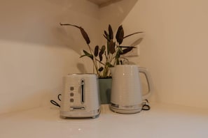 Een witte toaster en een witte mok op een witte aanrecht, met een potplant op de achtergrond.