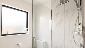 A modern bathroom with a toilet, a glass shower enclosure, and a window with a view. - The City Sanctuary | 4BR | 4 Baths | CBD (Christchurch)