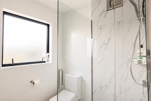 A modern bathroom with a toilet, a glass shower enclosure, and a window with a view.