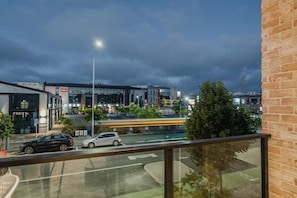 Vue depuis un balcon donnant sur un ensemble d’immeubles modernes à la façade vitrée, une rue avec des voitures et un pont en arrière-plan.