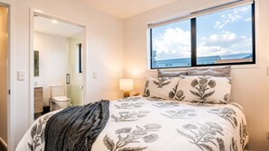 A bedroom with a bed, a window with a view, a bedside lamp, and a door leading to a bathroom. - The City Sanctuary | 4BR | 4 Baths | CBD (Christchurch)