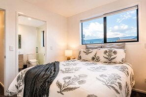 A bedroom with a bed, a window with a view, a bedside lamp, and a door leading to a bathroom.