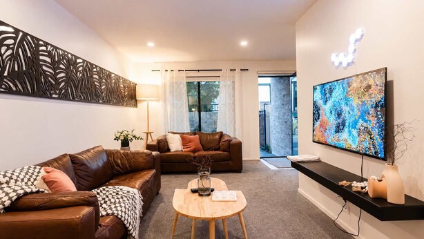 A modern living room with leather sofas, a coffee table, and a flat-screen TV mounted on the wall. - The City Sanctuary | 4BR | 4 Baths | CBD (Christchurch)