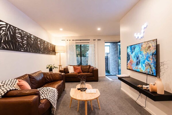 A modern living room with leather sofas, a coffee table, and a flat-screen TV mounted on the wall.