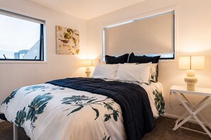 Une chambre à coucher avec un lit, une fenêtre, une œuvre d’art accrochée au mur et des lampes de chevet.