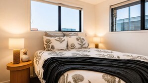 A bedroom with a bed, two bedside lamps, a nightstand, and two windows.