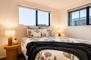 Une chambre à coucher avec un lit, deux lampes de chevet, une table de chevet et deux fenêtres.