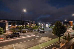 Une scène urbaine nocturne, avec un bâtiment moderne, des lampadaires et une voiture garée.