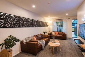 A living room with two brown leather sofas, a round wooden coffee table, a large abstract painting, and a decorative wall panel.