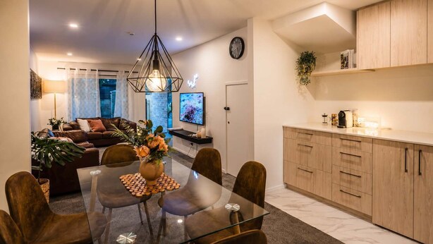 A modern living space with a dining area, a sofa, a TV, and a kitchen area.