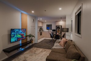 Un saló modern amb televisió de pantalla plana, un sofà, una taula de centre i una zona menjador amb cadires.