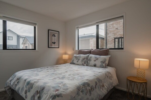 Une chambre à coucher avec un lit, deux tables de chevet, une fenêtre et un tableau accroché au mur.