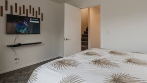 Une chambre moderne avec un lit, un téléviseur fixé au mur et une porte donnant sur un escalier.