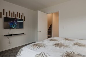Un dormitori modern amb un llit, televisió penjada a la paret i una porta que dona a una escala.