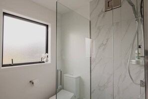 Un baño moderno con cabina de ducha de vidrio, inodoro y ventana con vistas.