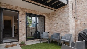 Un espace extérieur aménagé en patio, avec un mur en briques, un coin salon abrité et une porte donnant accès à un espace intérieur.