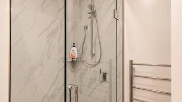 Eine moderne Dusche mit Duschbrause und einer Flasche Shampoo auf einem Regal.