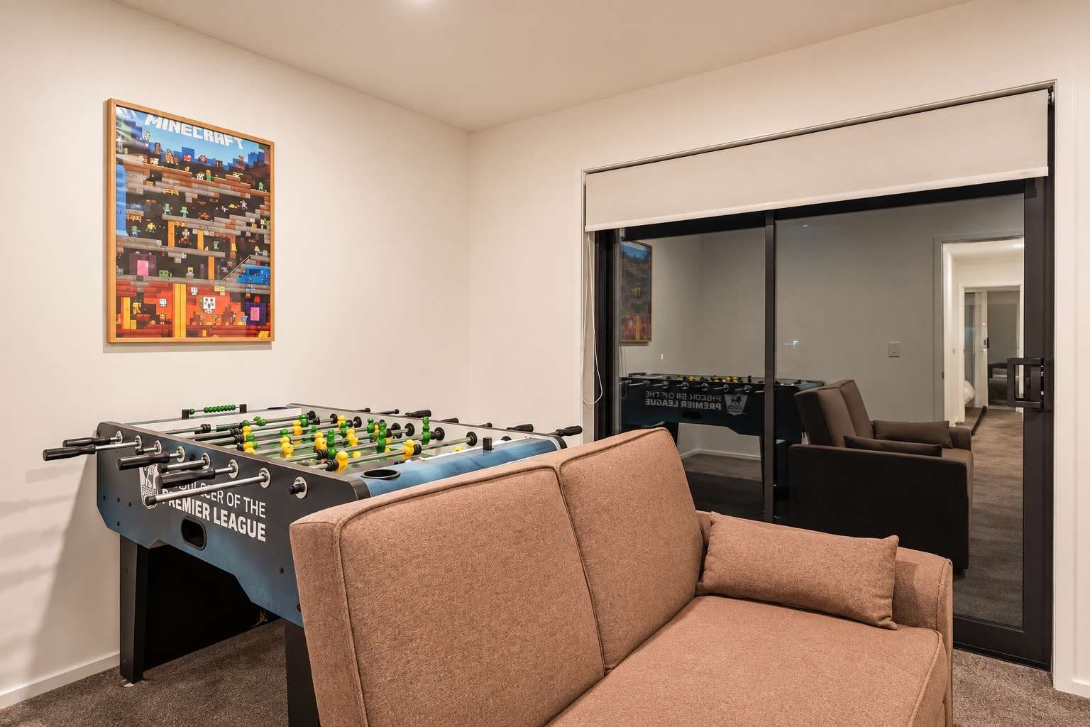 A room with a foosball table, a sofa, and a door leading to another room.