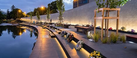 Un espace commémoratif extérieur paisible, comprenant un bassin d’eau calme, des bancs et des compositions florales en hommage.