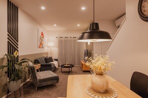 Ein modernes Wohnzimmer mit einer Couch, einem Esstisch mit einer Vase, einer Topfpflanze und einer Pendelleuchte.