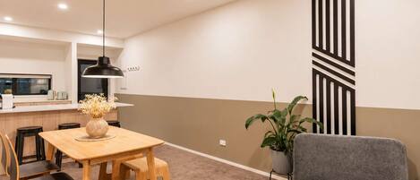 A modern living space with a dining area, a grey armchair, a potted plant, and a kitchen in the background.