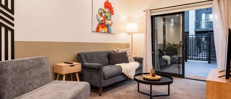 A modern living room with a grey sofa, a small side table, a coffee table, and a large window with a view of the outside.