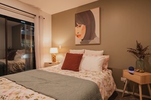 Une chambre d’hôtel avec un lit, une table de chevet avec une lampe, un vase de fleurs et un tableau au mur.