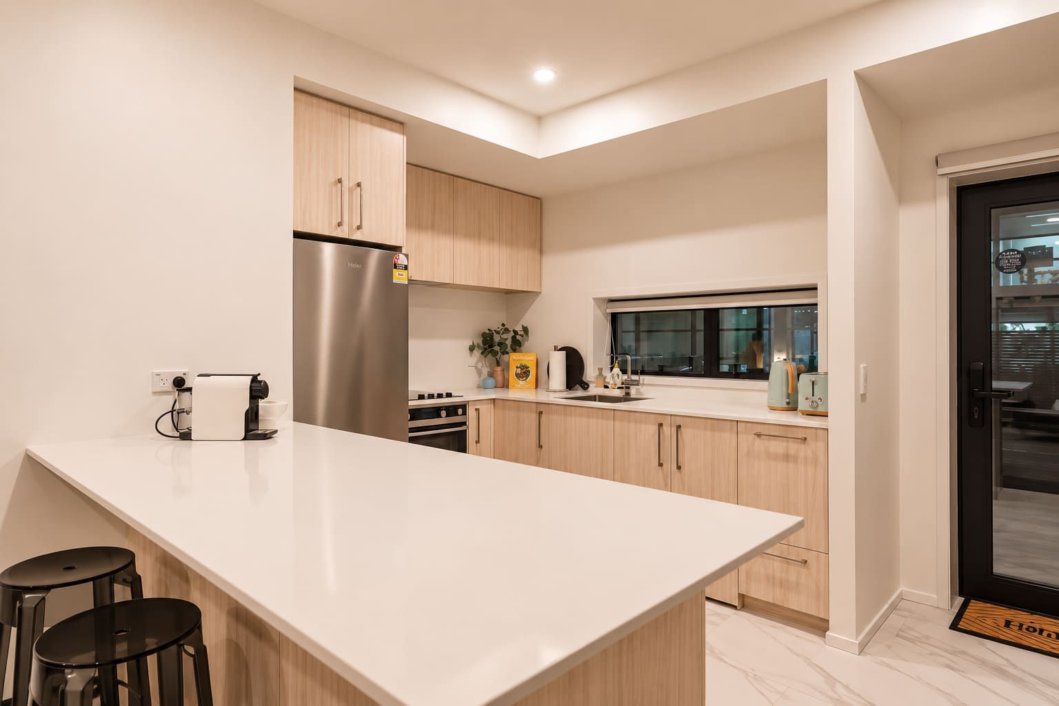 A modern kitchen with a large island, wooden cabinets, stainless steel appliances, and a window providing natural light.