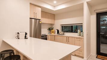 A modern kitchen with a large island, wooden cabinets, stainless steel appliances, and a window providing natural light.
