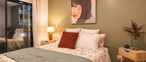 A hotel room with a bed, a nightstand, a lamp, a vase with flowers, and a painting on the wall.