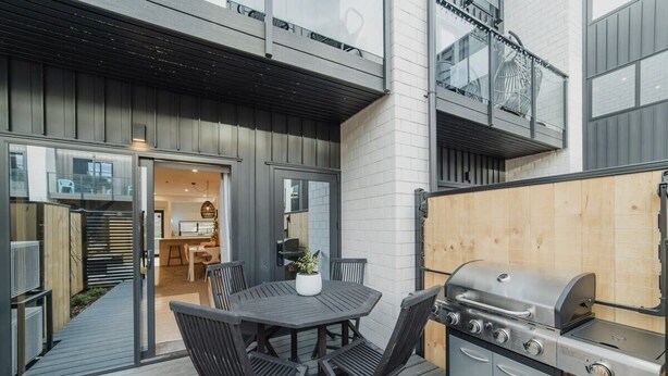 En udendørs patio med grill, et bord og stole, samt en træterrasse.