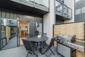Eine Terrasse im Freien mit Grill, Tisch und Stühlen sowie einem Holzboden.