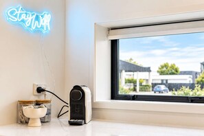 A room with a neon sign, a coffee machine, and a window with a view of buildings and cars.