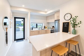 A modern kitchen with a large island, wooden cabinets, a stainless steel refrigerator, and a clock on the wall. - Riverside City Base | 4BR + BBQ | Group Stay (Christchurch Central City)