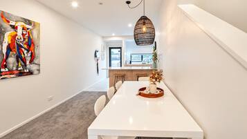 A modern kitchen with a white countertop, a hanging light fixture, and a dining area with a white table and chairs.