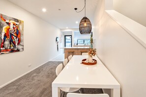 A modern kitchen with a white countertop, a hanging light fixture, and a dining area with a white table and chairs.