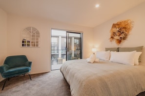 A bedroom with a bed, a chair, a window, and a view of buildings.