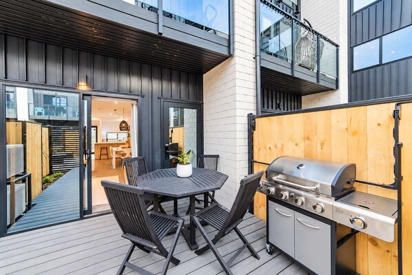 An outdoor patio with a grill, a dining table with chairs, and a view into the house.