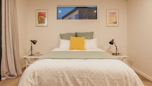 Une chambre à coucher bien rangée, avec un lit, deux tables de chevet, une fenêtre et deux tableaux encadrés accrochés au mur.