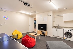 Un espace de vie compact comprenant une table de ping-pong, un téléviseur, un lave-linge et une petite cuisine.